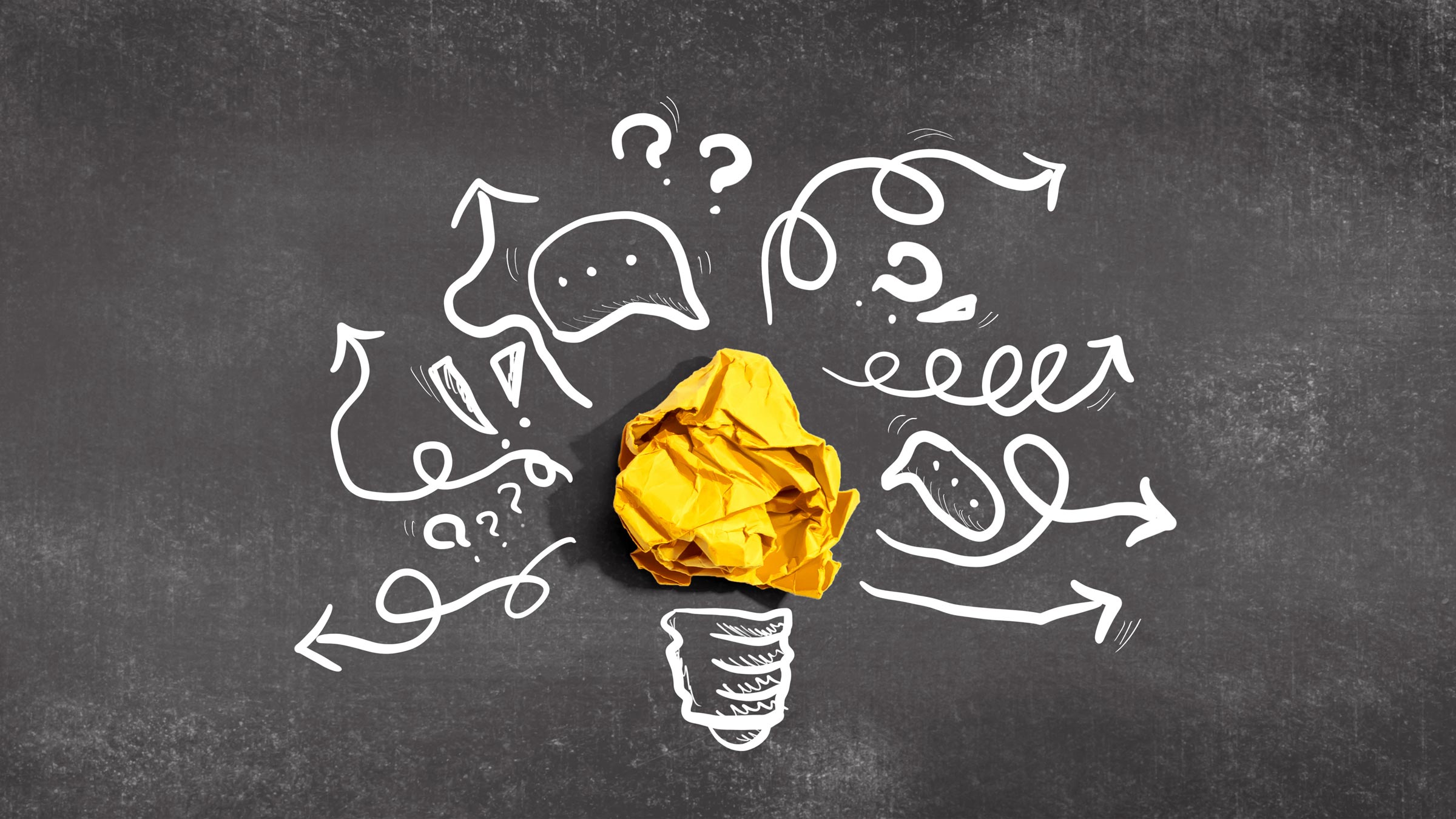Crumpled yellow paper shaped like a lightbulb surrounded by white doodles on a chalkboard background